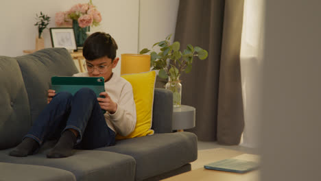 Kleiner-Junge-Sitzt-Zu-Hause-Auf-Dem-Sofa-Und-Spielt-Spiele-Oder-Streamt-Auf-Ein-Digitales-Tablet